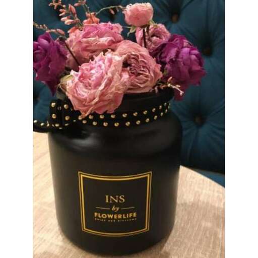 a vase of pink roses with a black lid and a gold ring on the front.