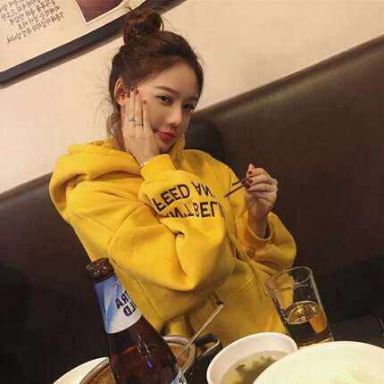 a woman in a yellow hoodie sitting at a table with a bowl of soup.