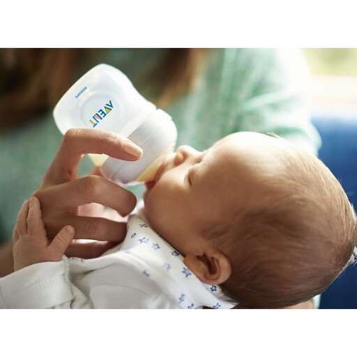 a baby drinking from a bottle while being fed.