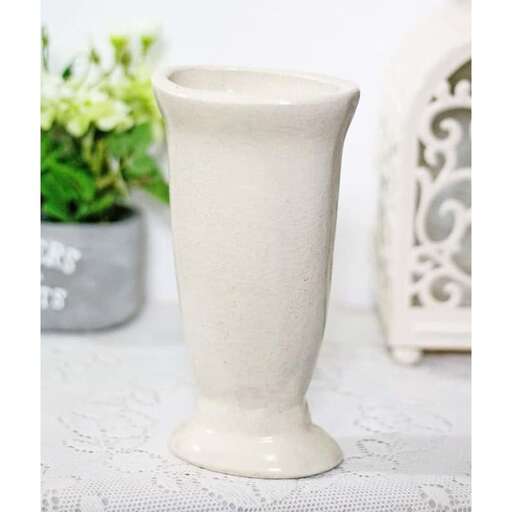 a white vase sitting on a table with a plant in the background.