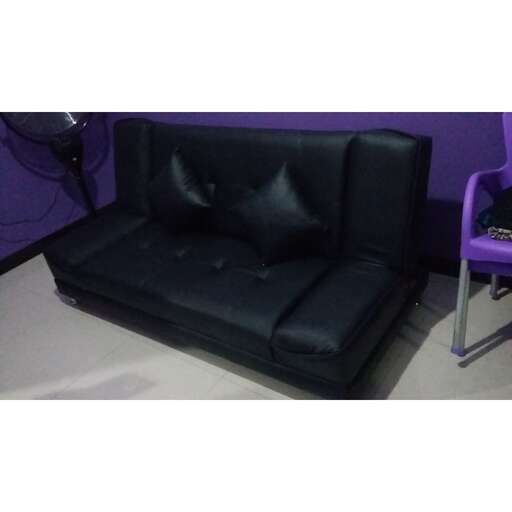 a black leather couch with a purple wall behind it.