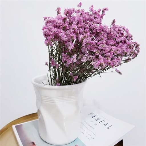 a white vase filled with purple flowers on a table.