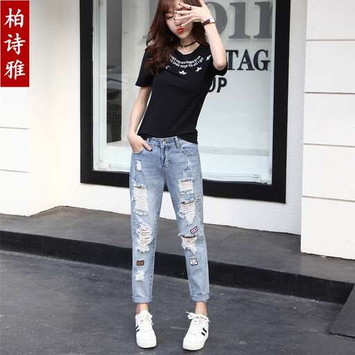 person, a fashion model, poses in a black t - shirt and ripped jeans.