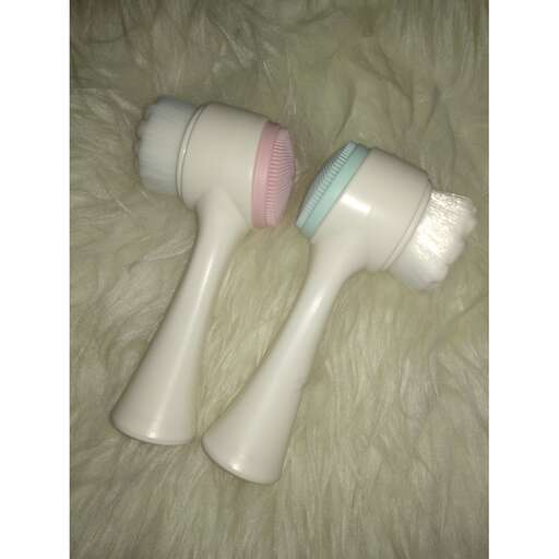 two toothbrushes laying on a white fuzzy blanket.