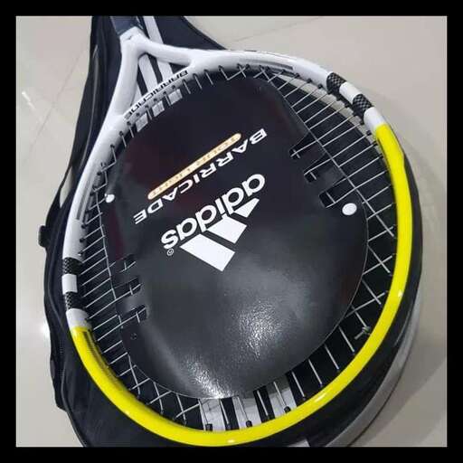 a tennis racket with a yellow rim is sitting on a tennis court.