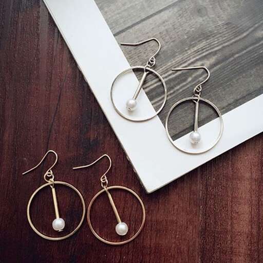 a pair of earrings with a white pearl on a wooden surface.