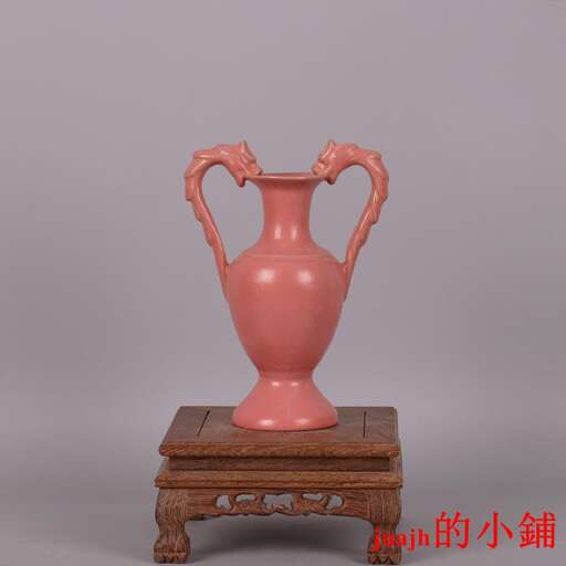 a pink vase with handles on a wooden stand