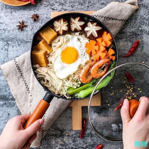 a person holding a frying pan with vegetables and meat.