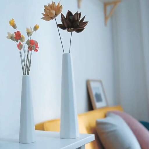 a white vase with flowers in it sitting on a table.