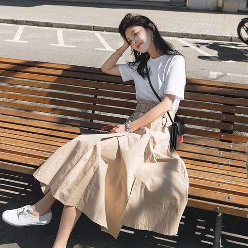 a woman sitting on a bench in a skirt and shoes.