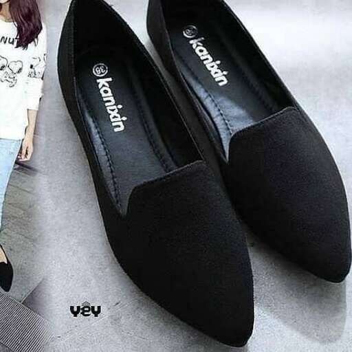 a woman standing next to a pair of black shoes.