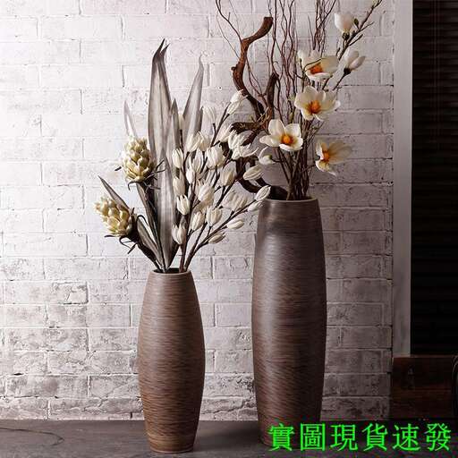 a large vase with flowers in it and a white wall behind it.