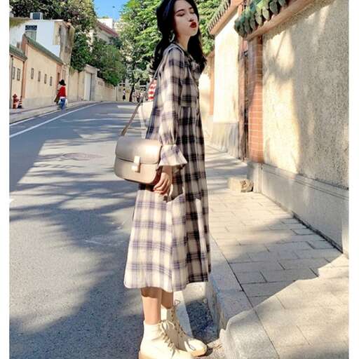 a woman in a plaid dress standing on a sidewalk.
