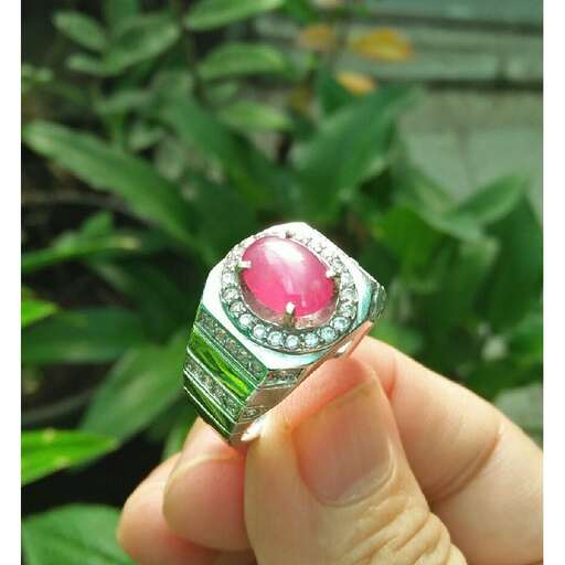 a hand holding a pink sapphire ring in a garden.