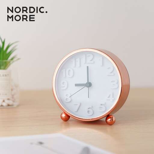 a pink clock with a white vase on a table.