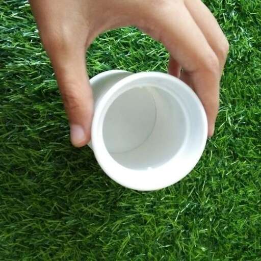 a hand holding a plastic cup on a green grass field.