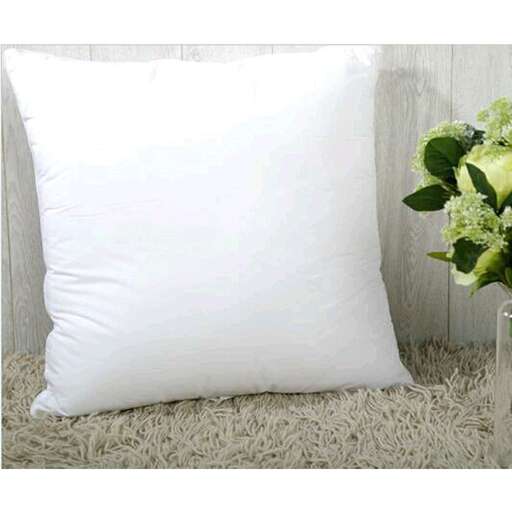 a white pillow sitting on a rug next to a vase of flowers.