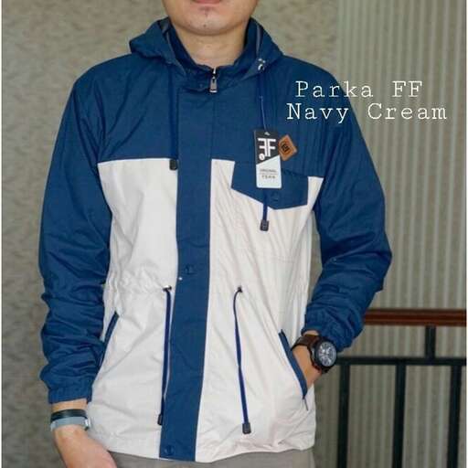 a man in a blue and white jacket standing in front of a wall.