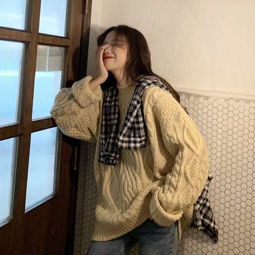 a woman leaning against a wall with a sweater on.