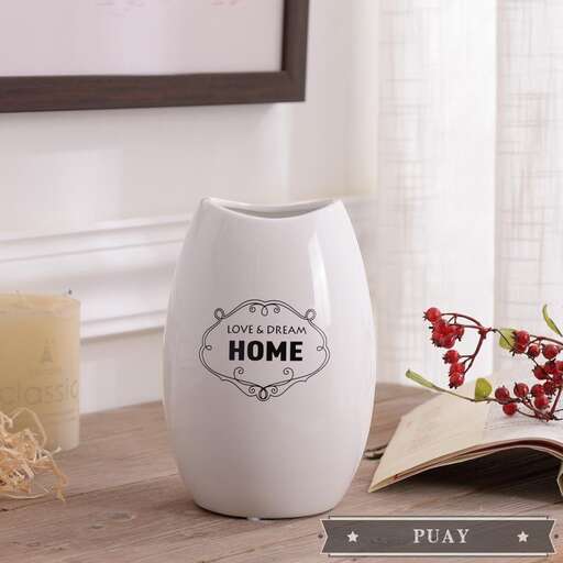 a white vase sitting on a table next to a candle.