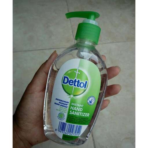 a hand holding a bottle of soap with a green lid.
