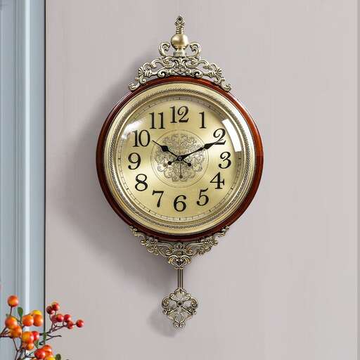 a gold clock hanging on a wall with a flower arrangement.
