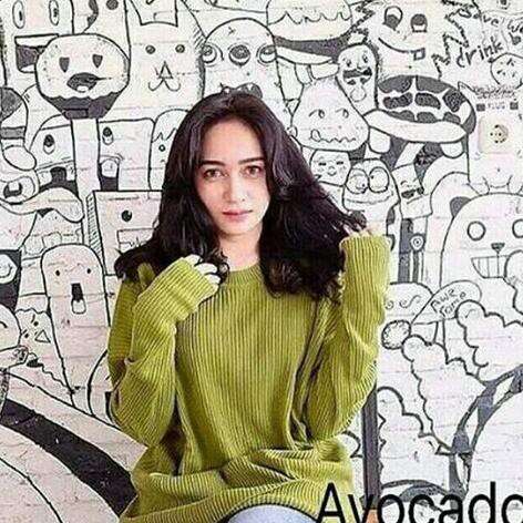 a girl in a green sweater sitting in front of a wall with a cartoon character.