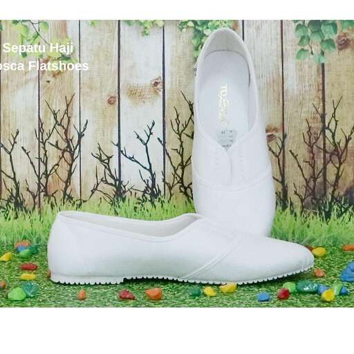 a pair of white shoes on grass with flowers in the background.