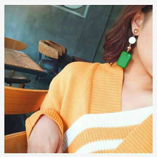 a woman wearing a yellow sweater and green earrings.
