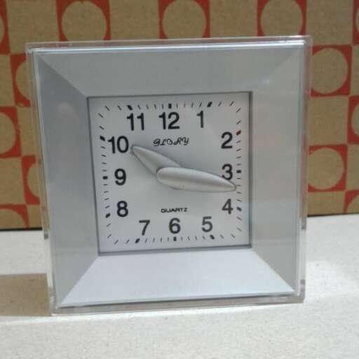 a square clock with a silver face is shown.