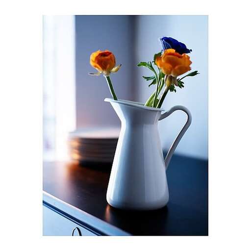 two orange roses in a white pitcher on a table.