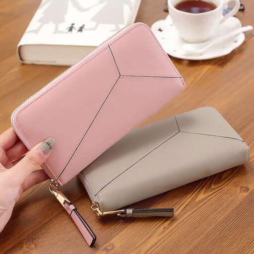 a hand holding a small wallet on a wooden table.