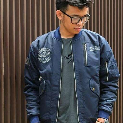 a man wearing a jacket and glasses standing in front of a metal wall.