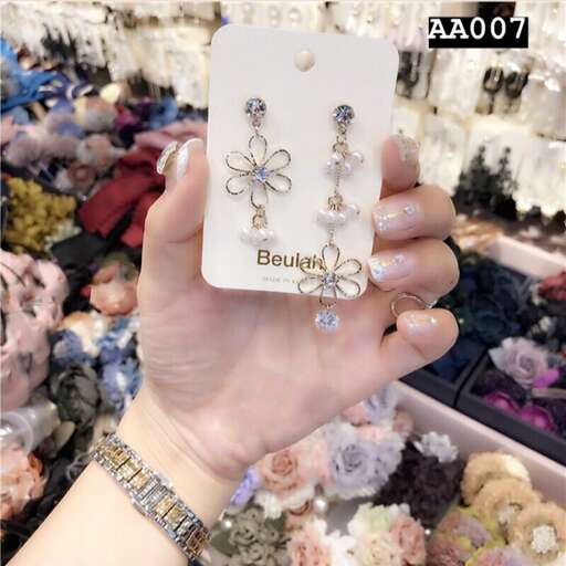 a hand holding a pair of earrings with a flower on top.