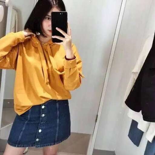 a woman in a yellow shirt taking a selfie in a mirror.