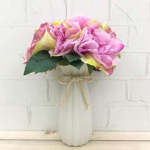 a white vase filled with pink flowers on top of a table.