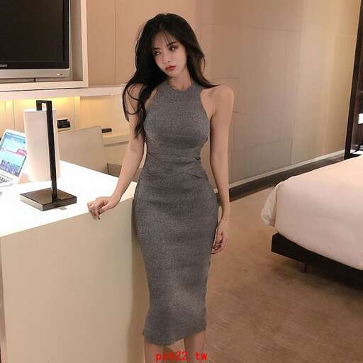 a woman in a grey dress standing next to a bed.