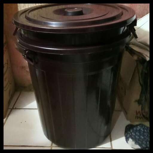 a black trash can sitting on a tile floor.