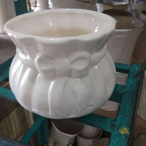 a white vase sitting on a table with a bow on it.