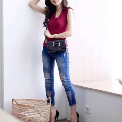 a woman poses in a red tank top and jeans.