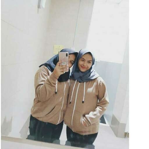 a girl in a hoodie and a scarf standing in front of a mirror.