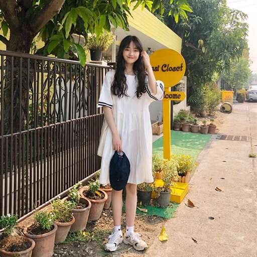 a girl in a white dress standing in front of a fence.