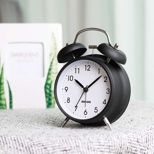 a black alarm clock sitting on a table next to a book.