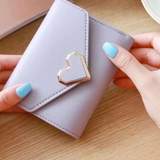 a woman's hand holding a heart shaped wallet with a gold heart on the front.
