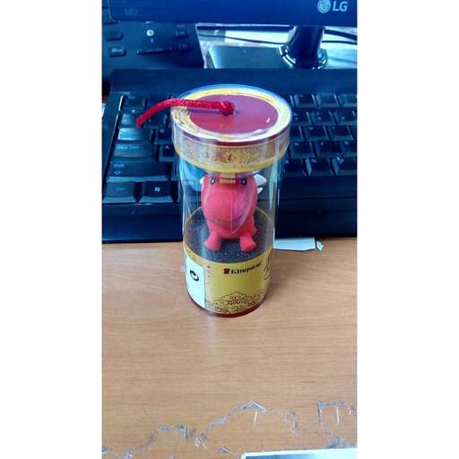 a jar with a red bird inside of it on a desk.