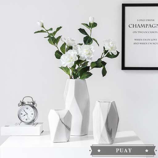 a white vase with flowers sitting on a table.