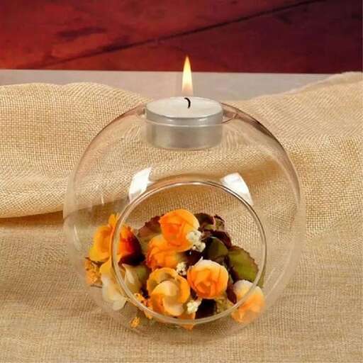 a candle in a glass bowl with dried flowers