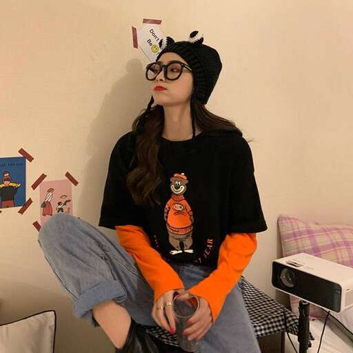 a girl in a black hat and orange shirt sitting on a chair.